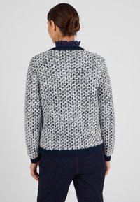 Pullover lavorato a maglia con un motivo in crema e blu marino testurizzato, caratterizzato da un colletto blu marino arricciato e polsini aderenti. La vista posteriore mostra un orlo blu marino uniforme.