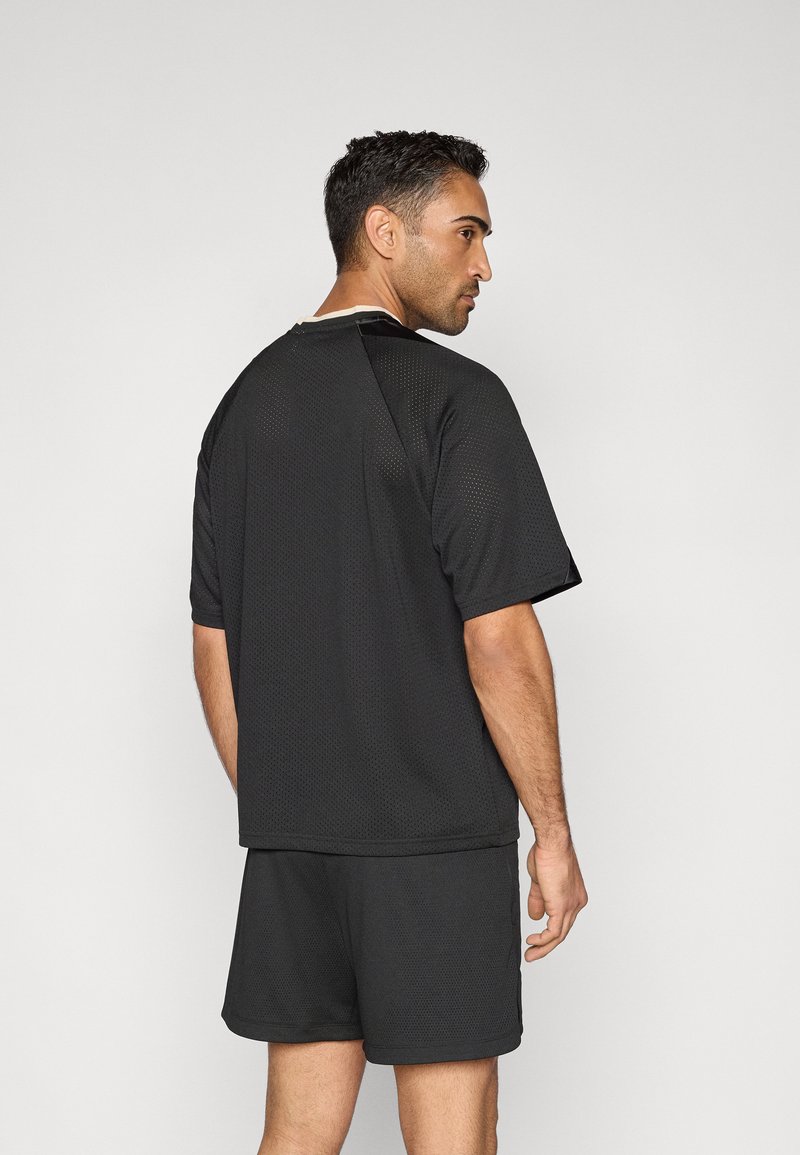 Svart sportskjorta i texturerat meshtyg, korta ärmar och avslappnad passform, kombinerad med matchande svarta shorts.