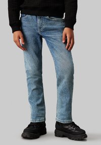 Jeans in denim blu chiaro con una vestibilità regolare, caratterizzati da un leggero sbiadimento, un design a cinque tasche e orli consumati, abbinati a scarpe nere con suola spessa.