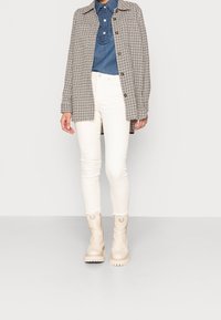 Rutig skjortjacka i beige och brunt, denimskjorta, vita tajta jeans och krämfärgade ankelboots med spänne.