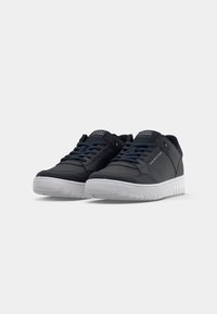 Une paire de baskets basses Tommy Hilfiger bleu marine avec des semelles et des lacets blancs, légèrement inclinée à droite sur un fond blanc.