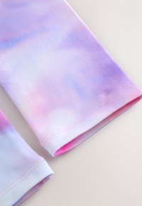 Pančuchy vyrobené z hladkej, pružnej látky s ružovo-modrým tie-dye vzorom. Zaoblené okraje s kontrastným šitím.