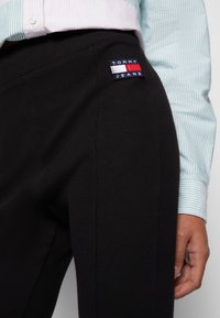 Černé žebrované jogger kalhoty s fitted designem. Obsahují malou, barevnou nášivku s logem Tommy Jeans na boku. Doplněné o světle modrou pruhovanou košili.