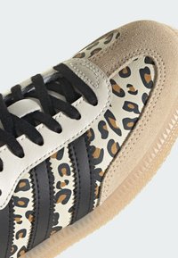 Tenis w panterkę z czarnymi paskami, jasnobrązowymi zamszowymi wstawkami i białą skórą. Odsłonięte sznurowadła i teksturowana gumowa podeszwa.