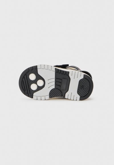 Semelle de sneaker noire et grise avec un motif texturé, comportant trois zones de grip circulaires et un accent blanc. Matériau en caoutchouc robuste.