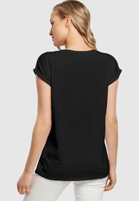 Sort t-shirt med korte oprullede ærmer, en afslappet pasform og en glat tekstur, båret med lyse bukser. Ingen synlige mønstre eller accenter.