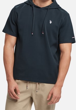 Sweat à capuche bleu marine à manches courtes avec cordons de serrage, présentant un petit logo sur la poitrine et un tissu texturé. Les accents incluent du rouge et du blanc sur les manches.