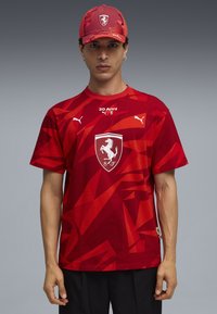 Rode T-shirt met een patroon, korte mouwen en een ronde hals, met een centraal logo en merkaccenten; gecombineerd met een bijpassende pet.