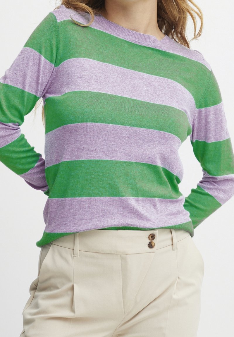 Maglione a maniche lunghe a righe verde e lavanda con scollo a girocollo, realizzato in un tessuto morbido. Pantaloni beige chiaro con doppio bottone.