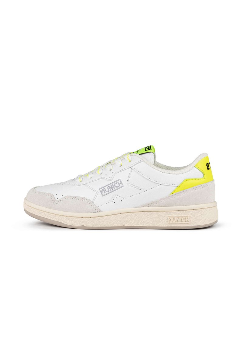 Zapatilla blanca con acentos de ante gris, detalles en amarillo y una suela de goma texturizada. Presenta un diseño de cordones y un logo en el costado.
