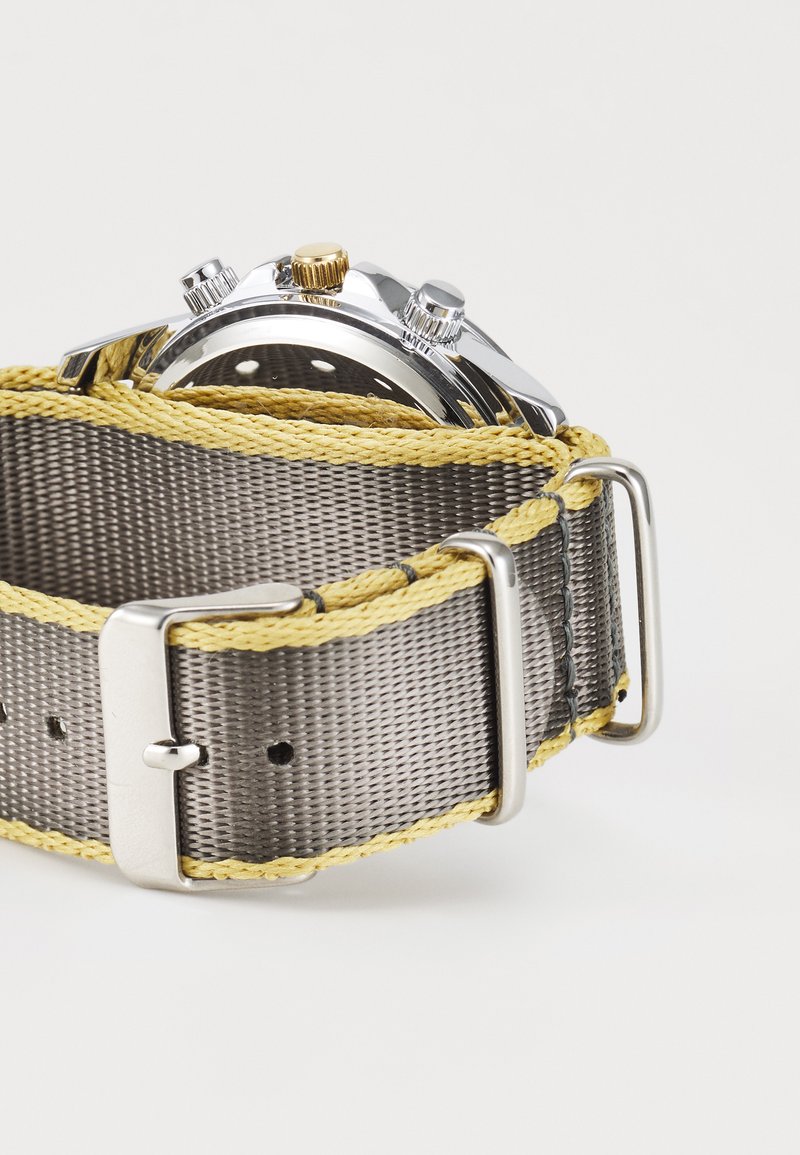 Montre chronographe avec un boîtier en argent, un bracelet tissé gris et des coutures jaunes. Dotée d'une quincaillerie en argent et en or, ainsi que d'une surface texturée.