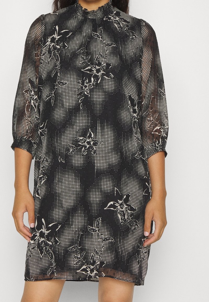 Robe noire transparente avec imprimé floral blanc et motif à pois, dotée de manches trois-quarts et d'un col montant froncé.