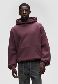 Felpa cappuccio bordeaux con grande tasca frontale, cappuccio con coulisse e branding minimale. Tessuto morbido con vestibilità rilassata e polsini a coste.