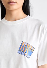 White cotton t-shirt with a round neckline featuring a blue and orange graphic logo on the left chest reading "tommy JEANS."