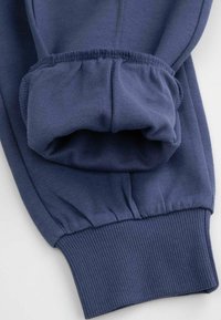 Granatowa koszula z długim rękawem z elastycznym ściągaczem i detalami w postaci zbieranych szwów, leżąca płasko na białym tle.