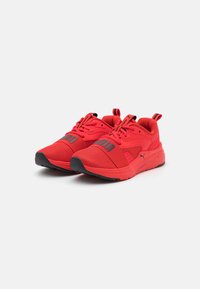 Red athletic shoes with mesh upper, contrasting black sole, and prominent logo. Features laces and pull tabs for easy wear.