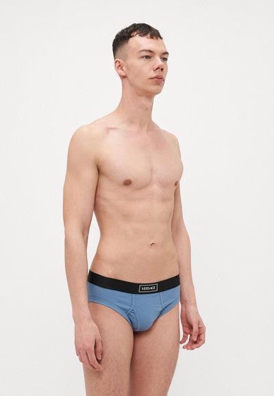 Culottes en coton bleu avec une ceinture noire arborant un logo. Le tissu a une texture lisse et le design est ajusté.