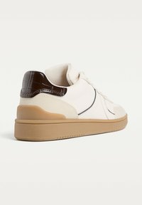 Baskets blanches basses avec semelle en caoutchouc beige et détail de talon en cuir crocodile brun foncé, vues d'un angle arrière.