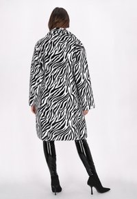 Cappotto in pelliccia sintetica con pattern a zebra bianco e nero, caratterizzato da una vestibilità comoda, maniche lunghe e colletto. Abbinato a leggings neri lucidi.
