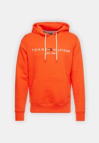 Sudadera con capucha naranja hecha de tela suave, con un bolsillo tipo canguro, cordones blancos y un logo con el texto "TOMMY HILFIGER" y "EST. 1985".