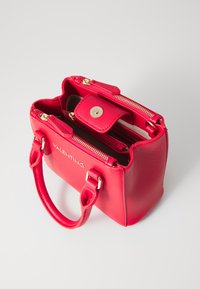 Sarkans ādas rokassoma ar zelta detaļām, divām augšējām rokturiem, ar rāvējslēdzēju un spiedpogu aizdari. Iekšējā daļa satur vairākus nodalījumus organizācijas nolūkos.