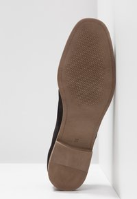 Sole di scarpa in suede nero con fondo in gomma testurizzata. Presenta una sezione del tacco liscia e marrone. Taglia contrassegnata come 37.