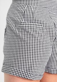 Černobílé krátké kalhoty s kostkovaným vzorem vyrobené z hladké látky, s bočními kapsami a srolovaným lemem na spodní části.