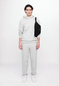 Grå sweatshirt og sweatpants-outfit med hvide sneakers. Slim-fit design; sweatshirten har hætte og minimal branding. Sort minimalistisk taske.