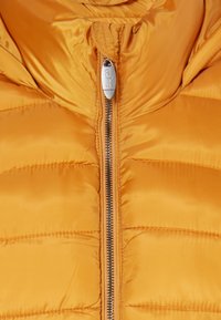 Žlutá pé�řová bunda s hladkým a lesklým povrchem. Má přední zip a prošívaný design, který zajišťuje tepelnou izolaci a kapuci.