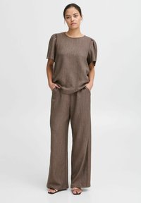 Braunes, strukturiertes Outfit mit einem kurzärmeligen Oberteil mit gerafften Schultern und weitem Hosenbein. Schlichtes Design mit subtilen Nähdetails.