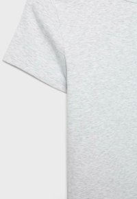 Tissu en coton gris clair d'un t-shirt à manches courtes en gros plan, montrant une texture lisse et des coutures fines sur la manche et la couture latérale.