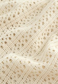 Tejido de ganchillo color crema con un patrón de cuadrícula abierta, que presenta formas hexagonales y de diamante, mostrando un acabado suave y texturizado.