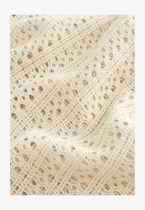 Tessuto all'uncinetto di colore crema con un motivo a lattice aperto, caratterizzato da forme esagonali e a rombo, che mostra una finitura morbida e testurizzata.