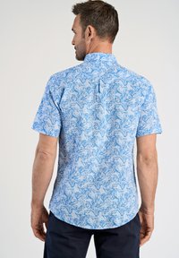 Korte mouwen shirt van lichtblauwe stof met een bloemenpatroon. Heeft een kraag en een ronde zoom met een rugplooidetail.