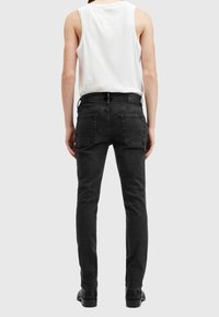 Černé džínové kalhoty slim fit s středně vysokým pasem, čtyřmi kapsami a jemným vybledlým odstínem, v kombinaci s bílým topem bez rukávů.