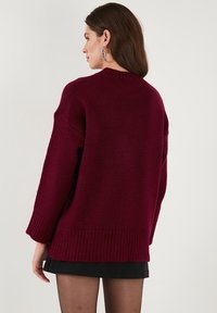 Bordó oversized pulóver ribbelések a hemnél és az ujjaknál, kerek nyakkal és vállnál lejjebb eső ujjakkal. Puha, texturált kötött anyag.
