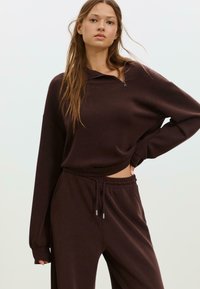 Hnědá fleecová mikina na zip s dlouhými rukávy a zkráceným střihem, doplněná o pasující kalhoty s elastickým pasem.