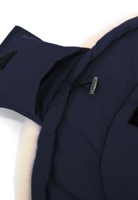 Marineblauwe buitenstof met zachte crème fleece voering, voorzien van klittenbandsluiting en een elastisch trekkoord met een metalen trekknop voor aanpassingen.