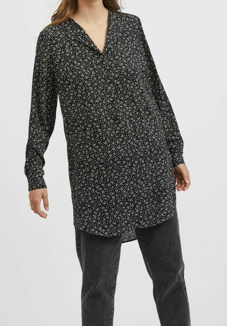 Svart långärmad blus med V-ringning, prickigt vitt blommönster och rundad nederkant. Matchad med mörka jeans.