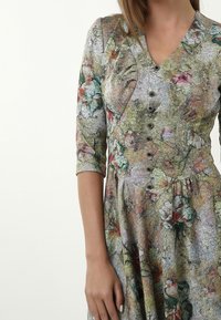Blumenmuster Kleid mit V-Ausschnitt, kurzen Ärmeln und Knopfdetails an der Vorderseite. Hergestellt aus leichtem, strukturiertem Stoff in gedämpften Farben.