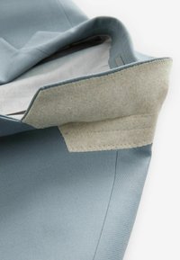Hellblaues Gewebe mit strukturierten Oberflächen. Das Innere besteht aus hellgrauem Filzmaterial mit genähten Akzenten. Sauber, modernes Design.
