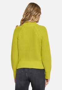 Limettengrüner, gestrickter Pullover mit hohem Kragen und gerippten Bündchen. Verfügt über ein strukturiertes Muster und eine lockere Passform, kombiniert mit dunkelgrauen Jeans.