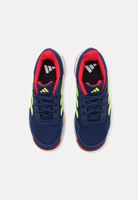 Zapatillas de malla azul marino con rayas verde lima, detalles rojos y plantilla negra. Presentan cordones estándar y suela de goma texturizada.