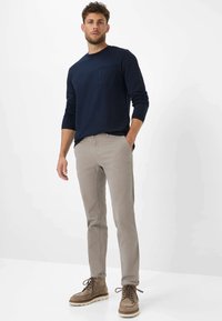 Navy long-sleeve shirt with a chest pocket, paired with light gray chinos and brown suede boots with white soles. Simple, clean design.