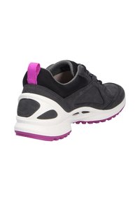 Scarpa sportiva nera realizzata in materiali scamosciato e mesh, con intersuola bianca, suola esterna viola e un tab sul tallone rosa. Presenta un collare imbottito e un sistema di allacciatura.