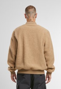 Tan sherpa-fleece pullover met een ontspannen pasvorm, ronde halslijn, geribbelde boorden en zoom, met een gestructureerd, pluizig oppervlak.
