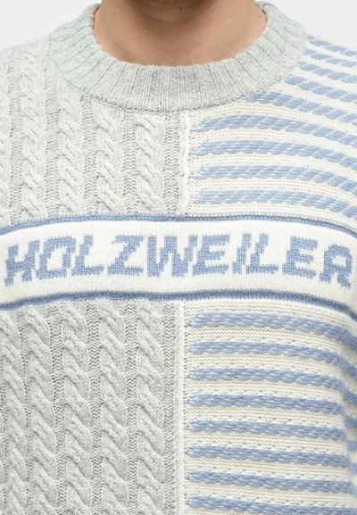 Szürke és krémszínű kötött pulóver, amely kábelmintával és vízszintes kék csíkokkal díszített, középen egy sávval, amelyen kék betűkkel a "HOLZWEILER" felirat olvasható.