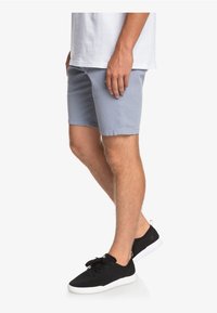 Světle modré šortky vyrobené z lehké tkaniny, s plochým předním dílem a bočními kapsami, kombinované s černými teniskami a bílým tričkem.