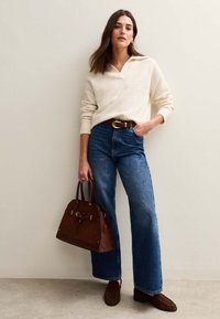 Kremowy sweter, spodnie dżinsowe z wysokim stanem w kolorze niebieskim, brązowa torebka, brązowe mokasynki, złota klamra paska, luźny krój, pionowa sylwetka.