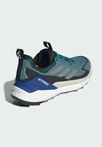Trail running shoe featuring a textured teal upper with gray accents, black heel, and blue branding. Lightweight sole with tread.